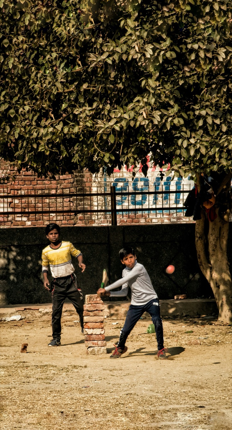 Boys playing cricket with brick wicket